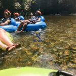 Group of travelers floating on inner tubes at Nohoch Che’en Caves Branch Archaeological Reserve in Belize.